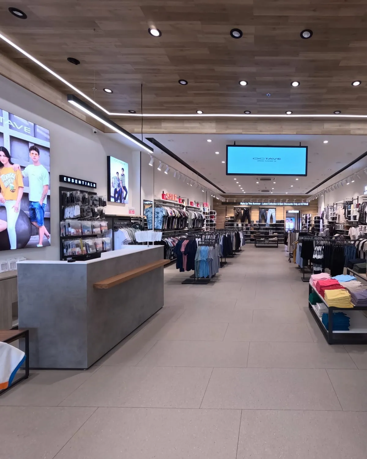Central aisle of the store, shelved menswear either side under track lighting.