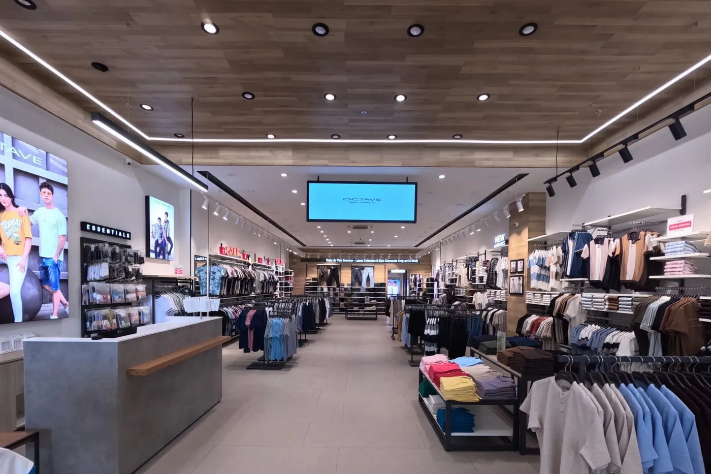 Central aisle of a fitted-out store, shelved menswear either side under track lighting.
